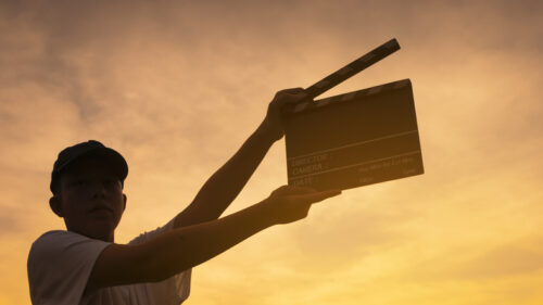 Un jeune réalisateur de cinéma tient un clap de tournage dans la lumière d'un coucher de soleil.
