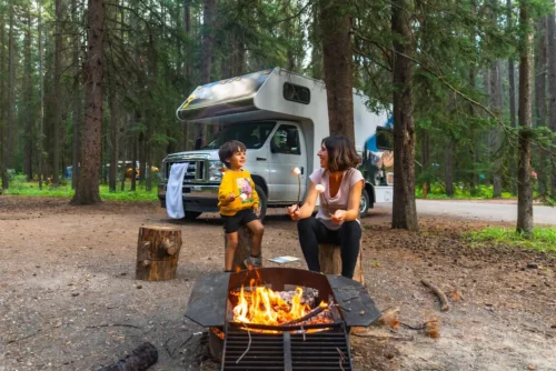 une mère et son fils grillent des marshmallows sur un feu de camp devant leur camping-car